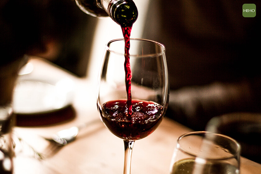 Red wine being poured into a stem glass at the table.
